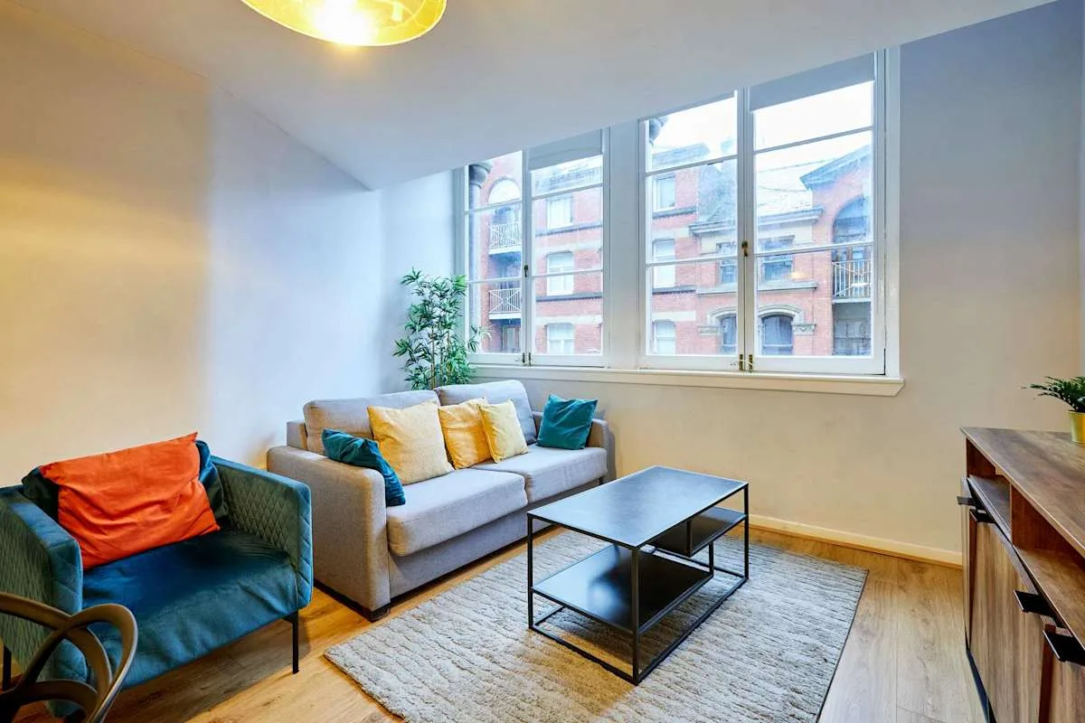 A living room with seating arranged around a coffee table beneath large windows.