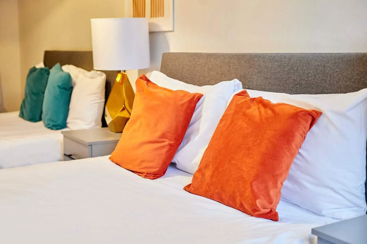 A bedroom with orange accent pillows on the bed and a bedside lamp.