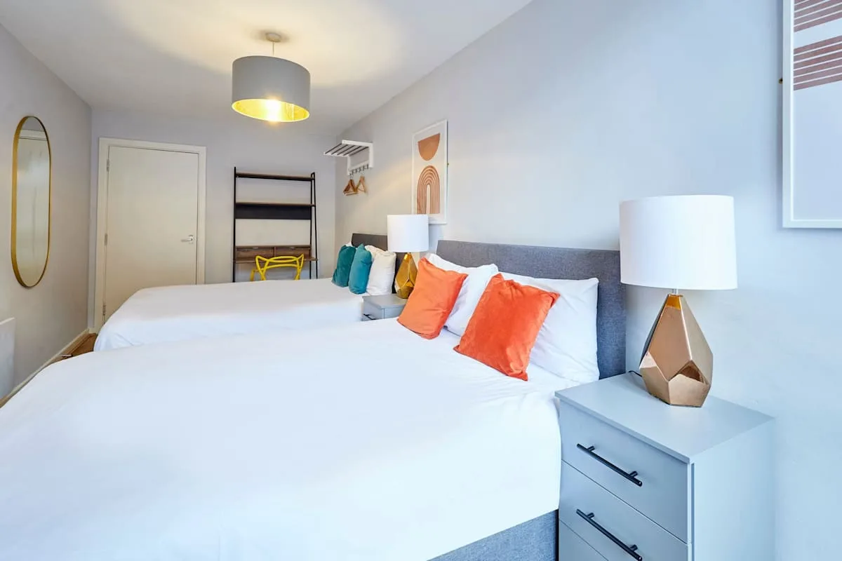 A bedroom with two beds, colorful cushions, and bedside lamps.