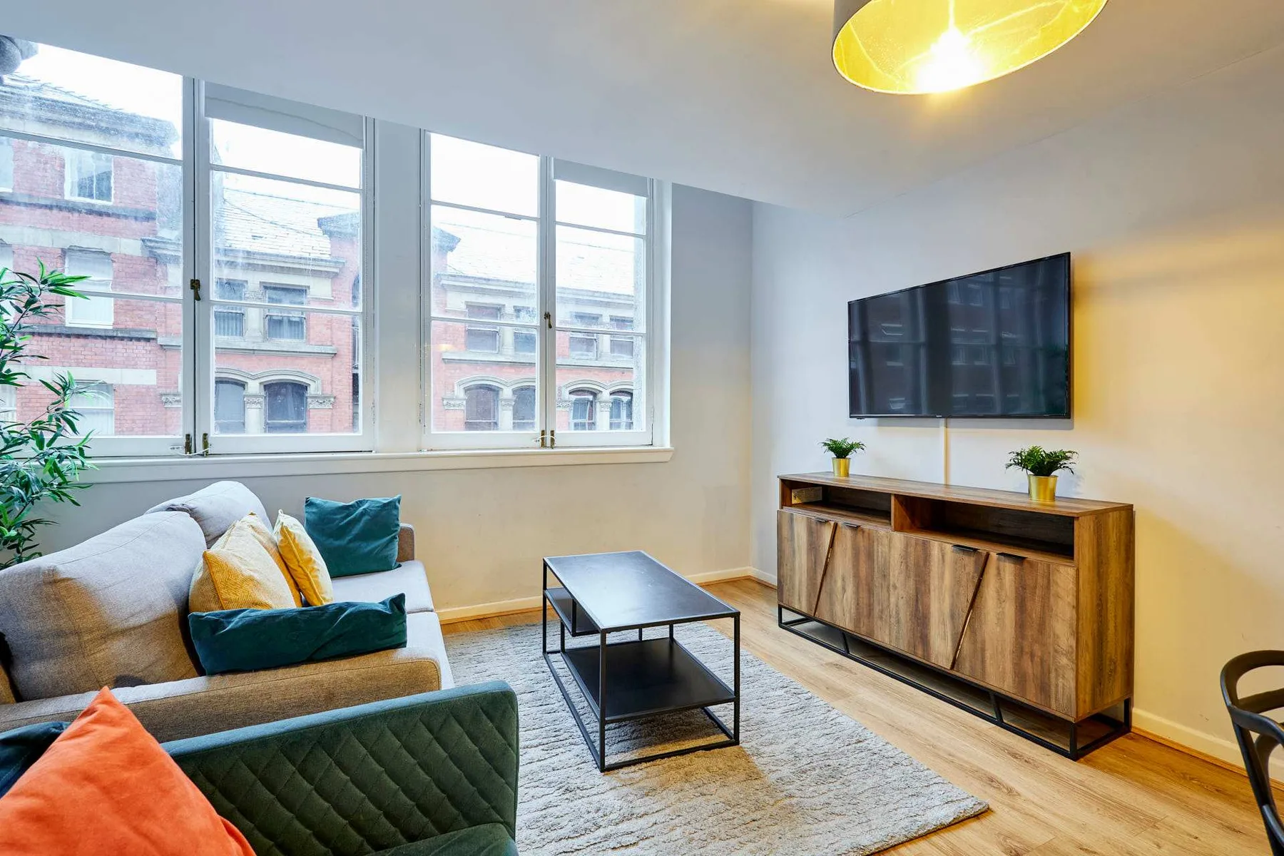 Una sala luminosa con asientos, una mesa de centro y un televisor sobre un mueble de madera.
