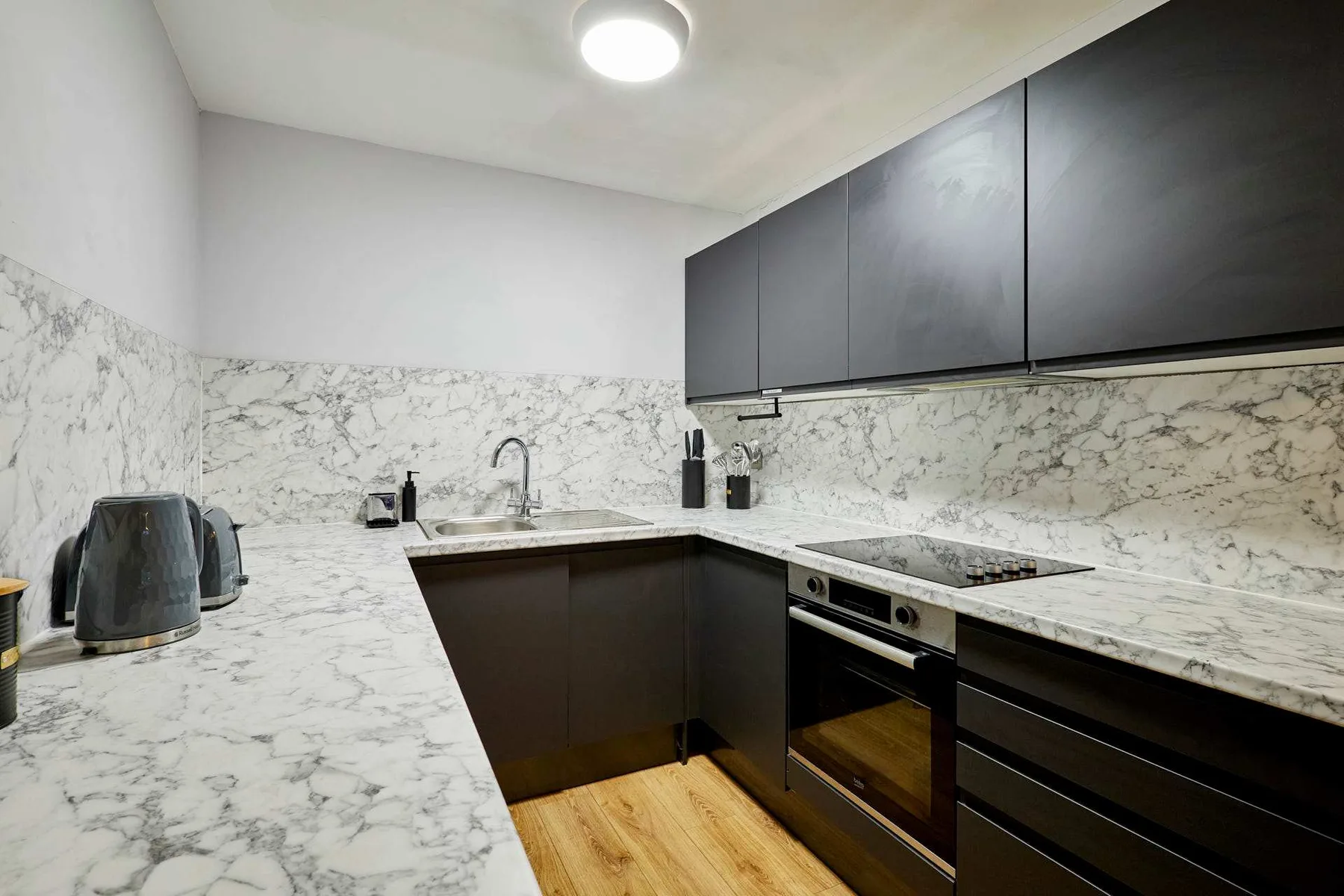A modern kitchen with dark cabinets, marble-patterned counters, and a built-in oven.
