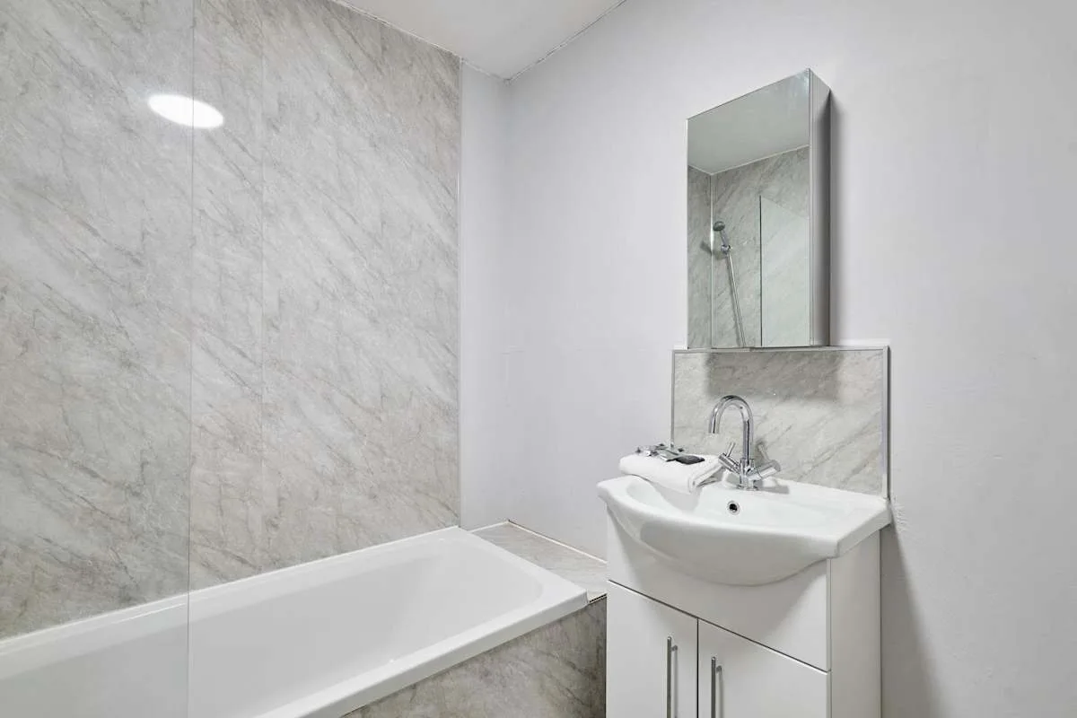 A bathroom with a bathtub, glass shower screen, and sink.