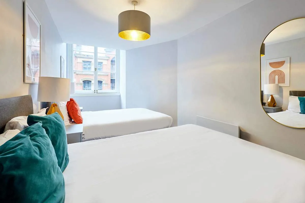 A bright bedroom with two beds and a window overlooking nearby buildings.