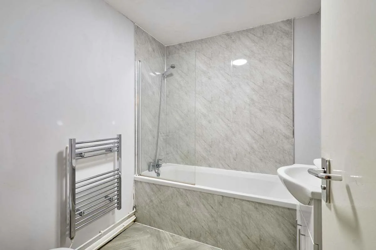 A bathroom with a bathtub, wall-mounted shower, and heated towel rail.