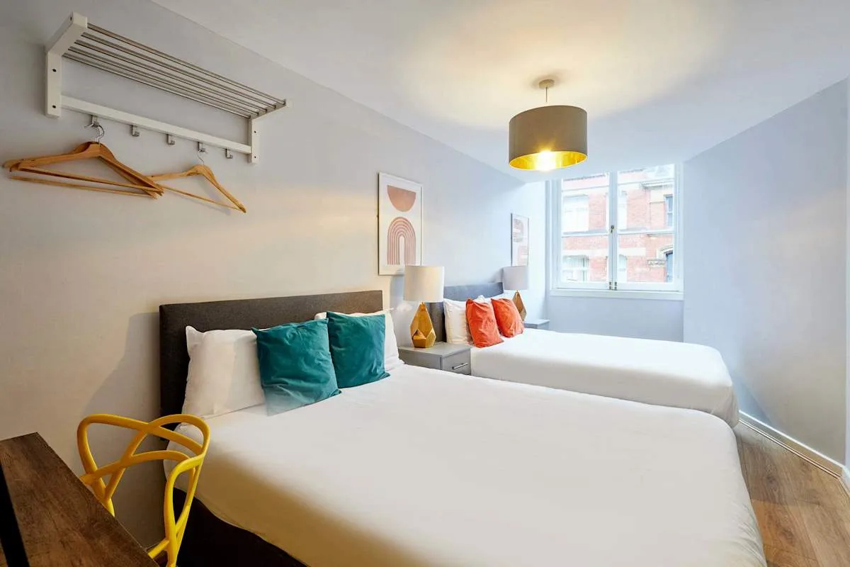 A bright bedroom with two beds and colorful accent pillows.
