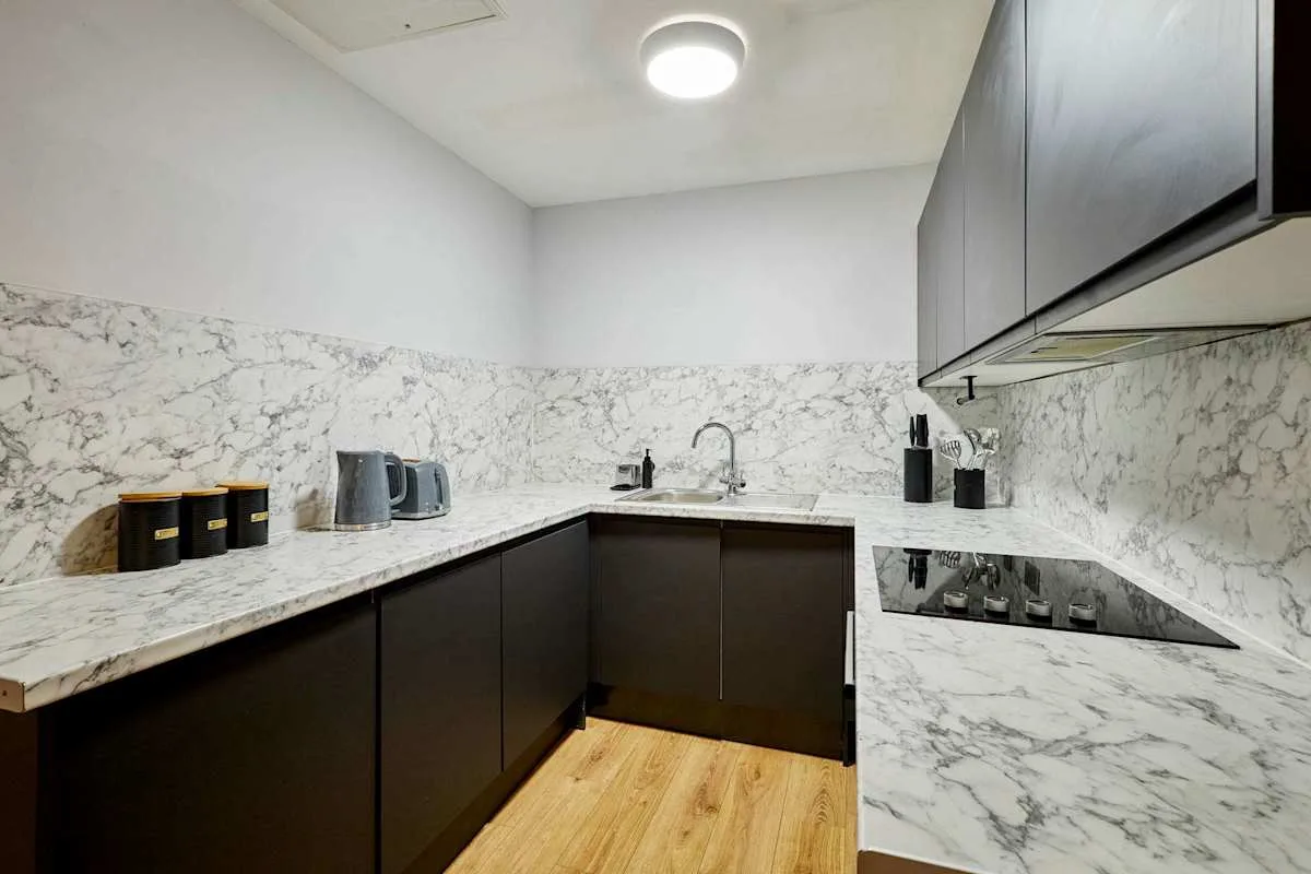 A modern kitchen with dark cabinets, marble-patterned surfaces, and a cooktop.