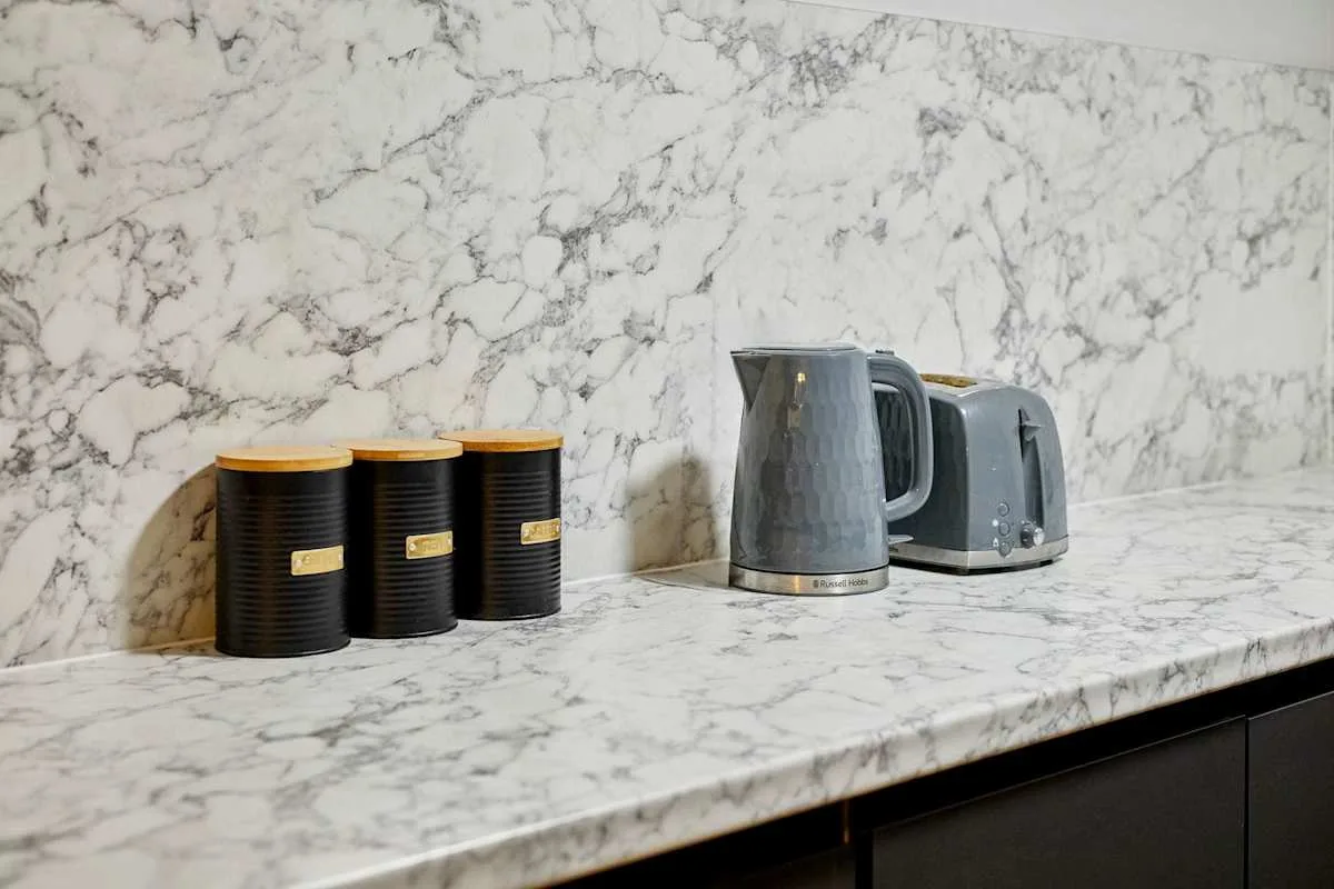 A kitchen counter with a kettle and canisters against a marble-patterned backsplash.
