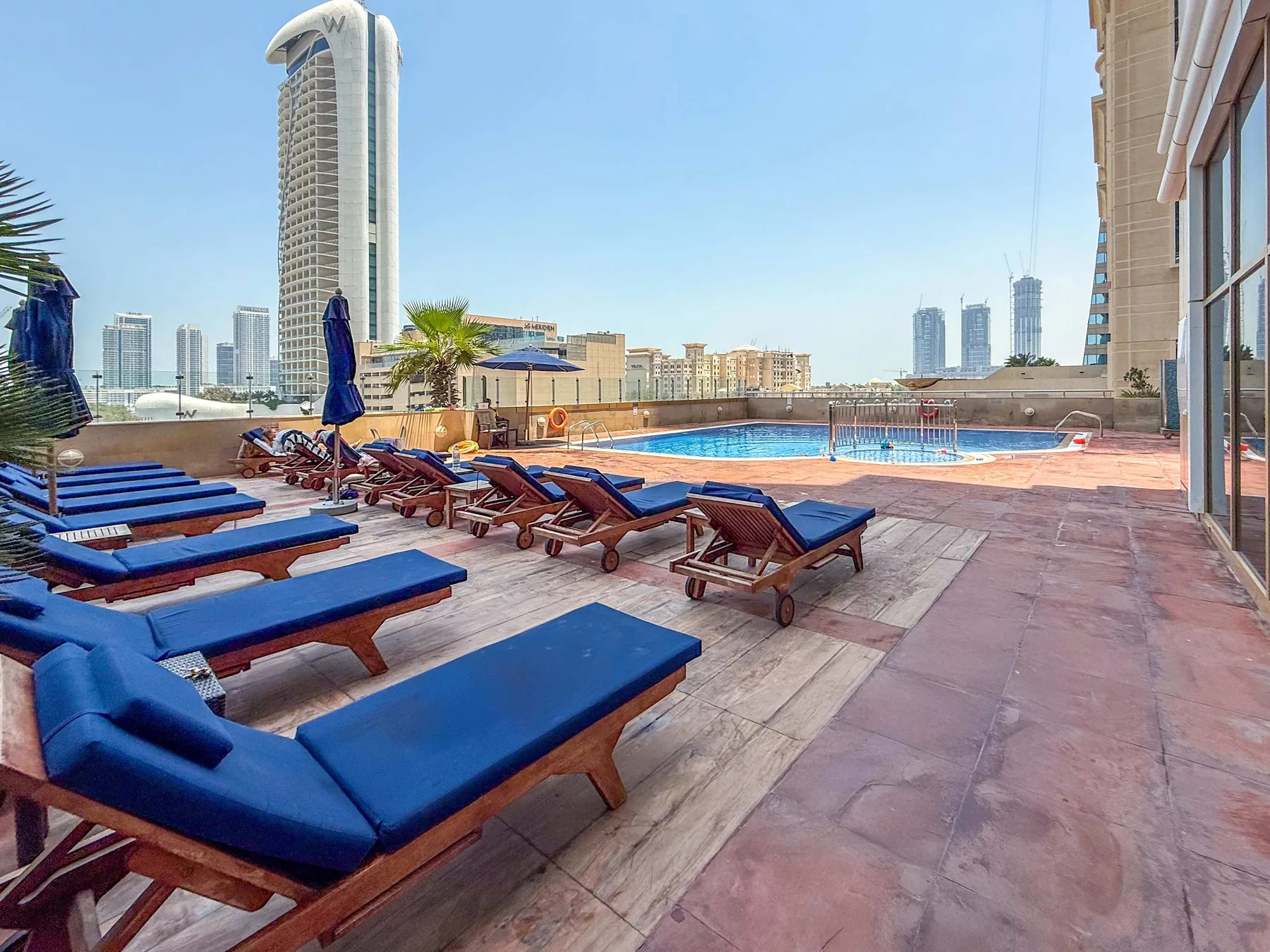 Una terraza con piscina y tumbonas azules ofrece vistas del horizonte urbano.