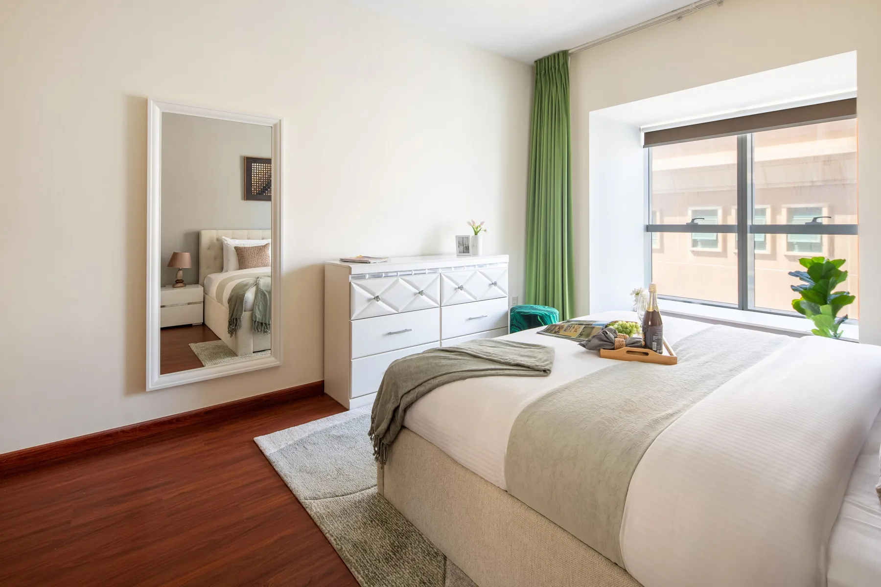 Un dormitorio luminoso con una cama bien arreglada, una cómoda blanca y una ventana grande.