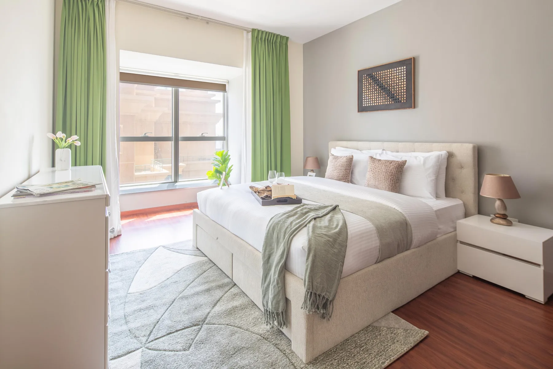 Un dormitorio luminoso con una cama bien tendida y cortinas verdes junto a una ventana grande.