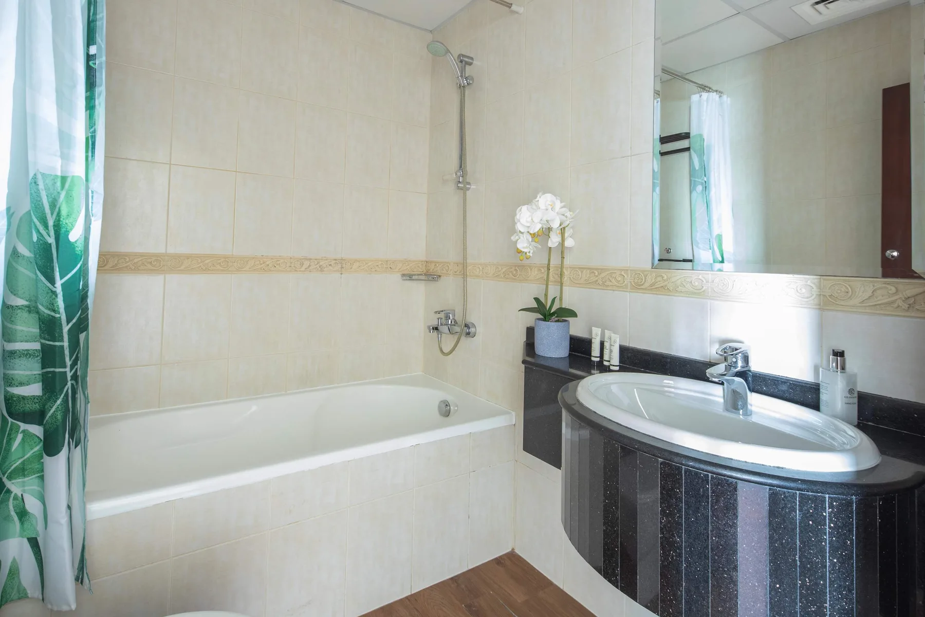 Baño alicatado con bañera, ducha y tocador curvo con lavabo.