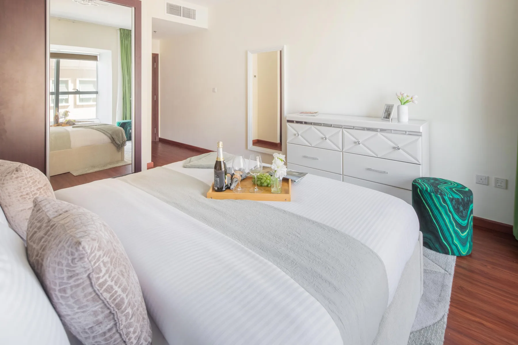 Un dormitorio luminoso con una cama bien hecha y una cómoda junto a la pared.