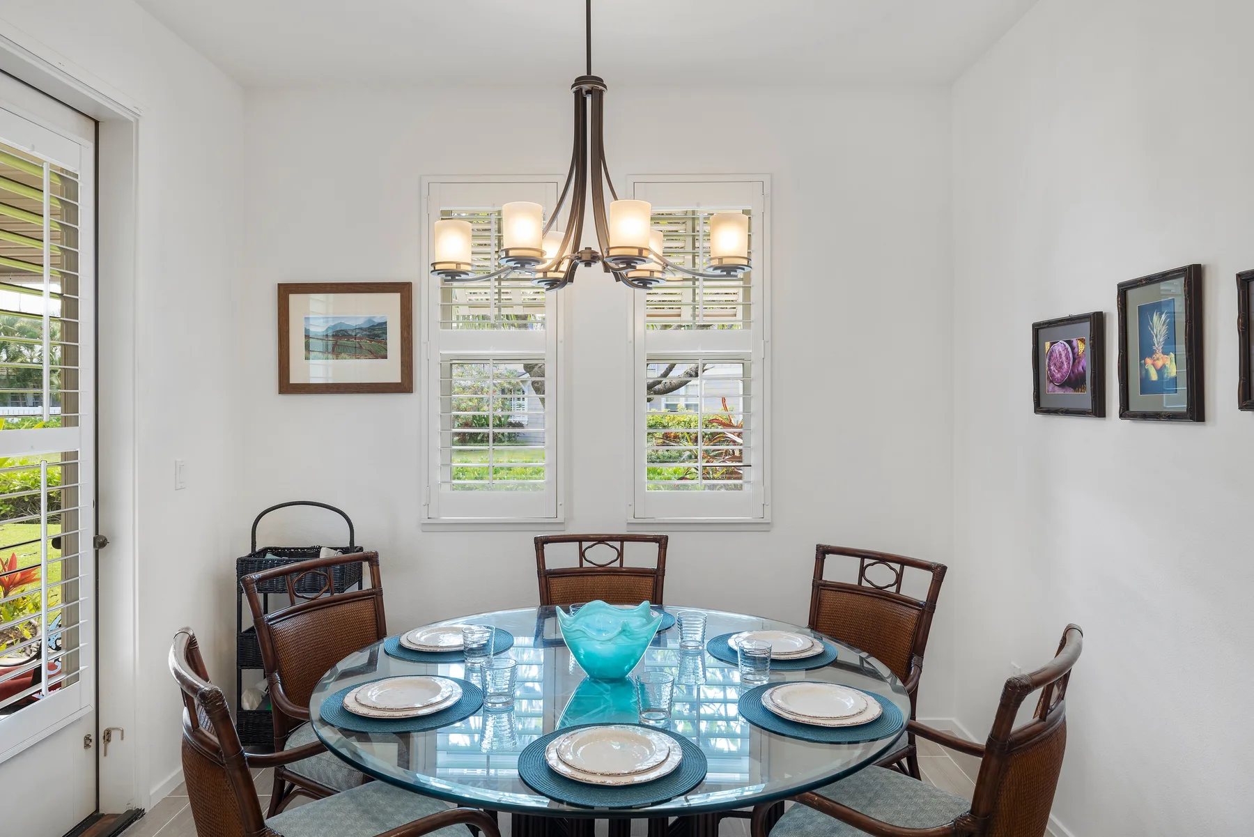 Un comedor luminoso con una mesa de vidrio y asientos de madera bajo una lámpara de araña.