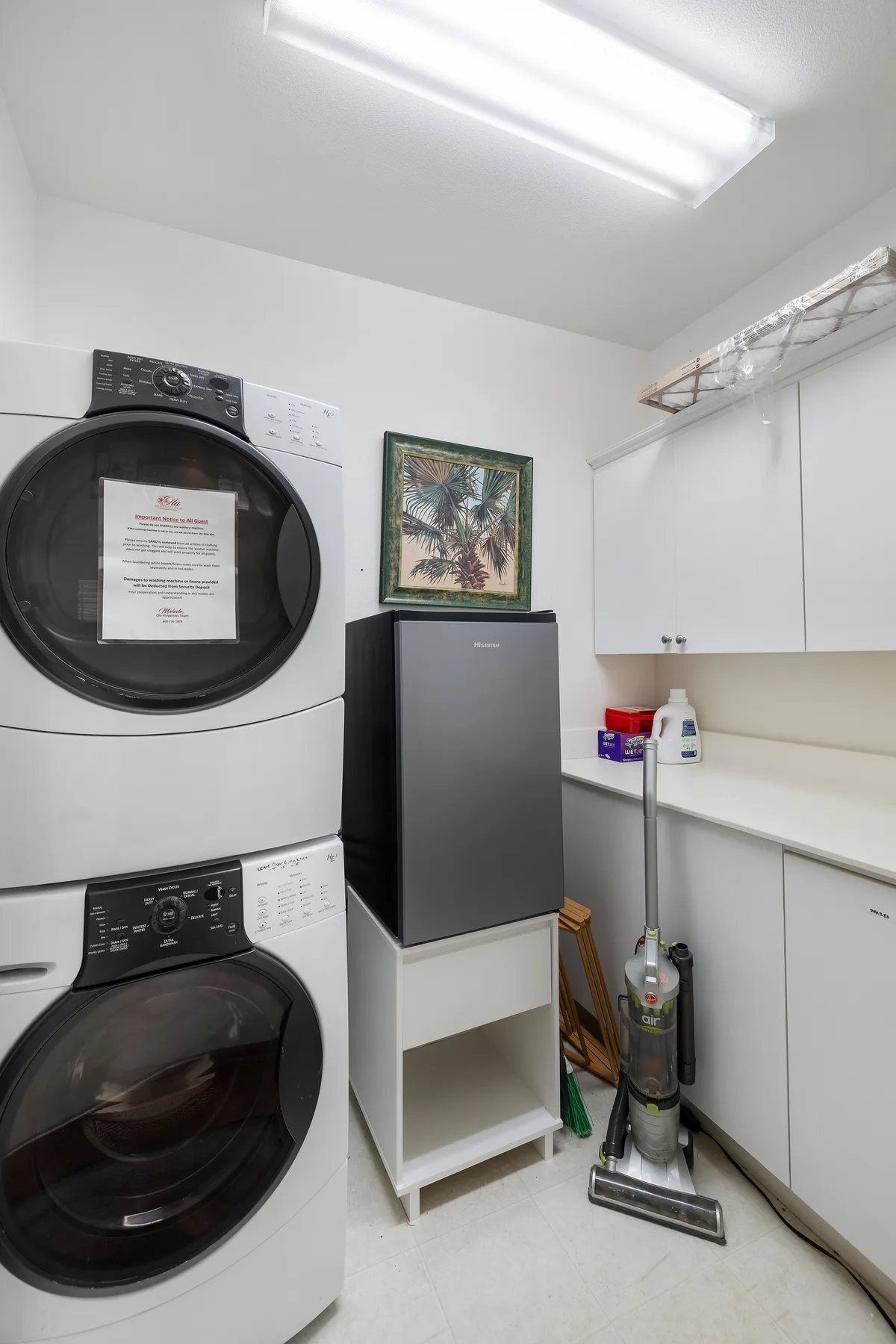 Un cuarto de lavandería con lavadoras apiladas, un refrigerador compacto y artículos de limpieza.