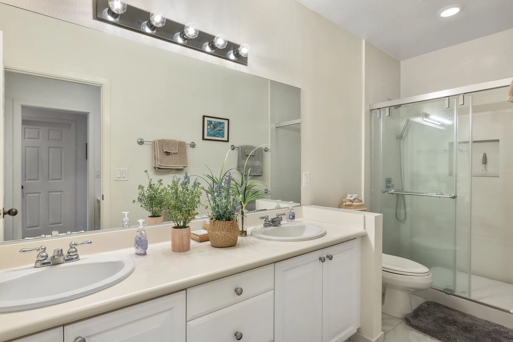 Un tocador de baño con un espejo grande está junto a una ducha de vidrio.