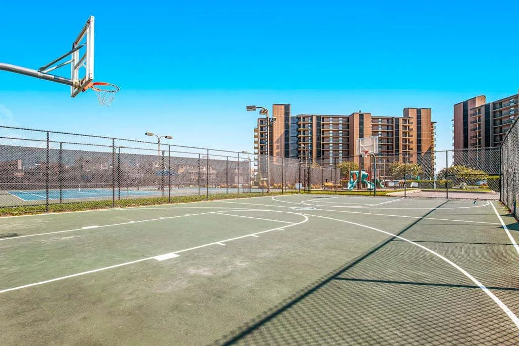 An outdoor basketball court with fenced courts and apartment buildings in the background.