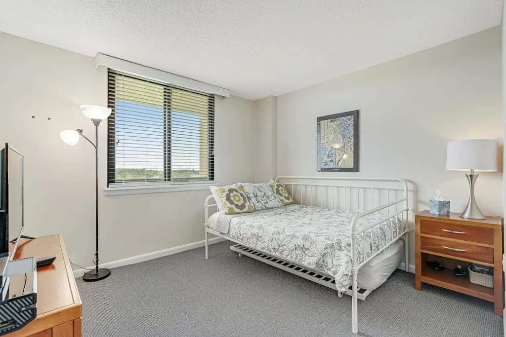 A bedroom with a daybed beneath a window with blinds.
