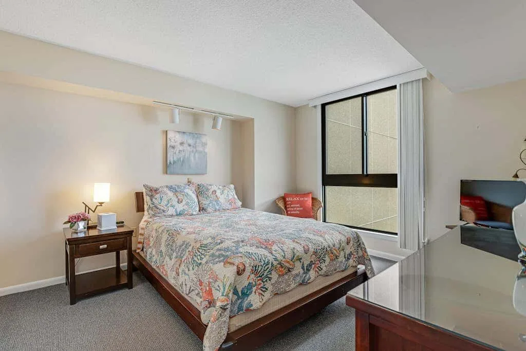 A bedroom with a patterned bedspread and a window beside the bed.