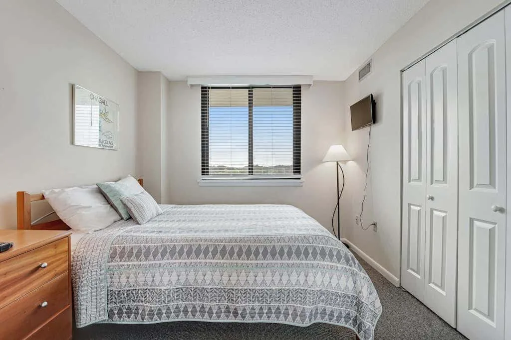 A bedroom with a bed beneath a window and a wall-mounted television.