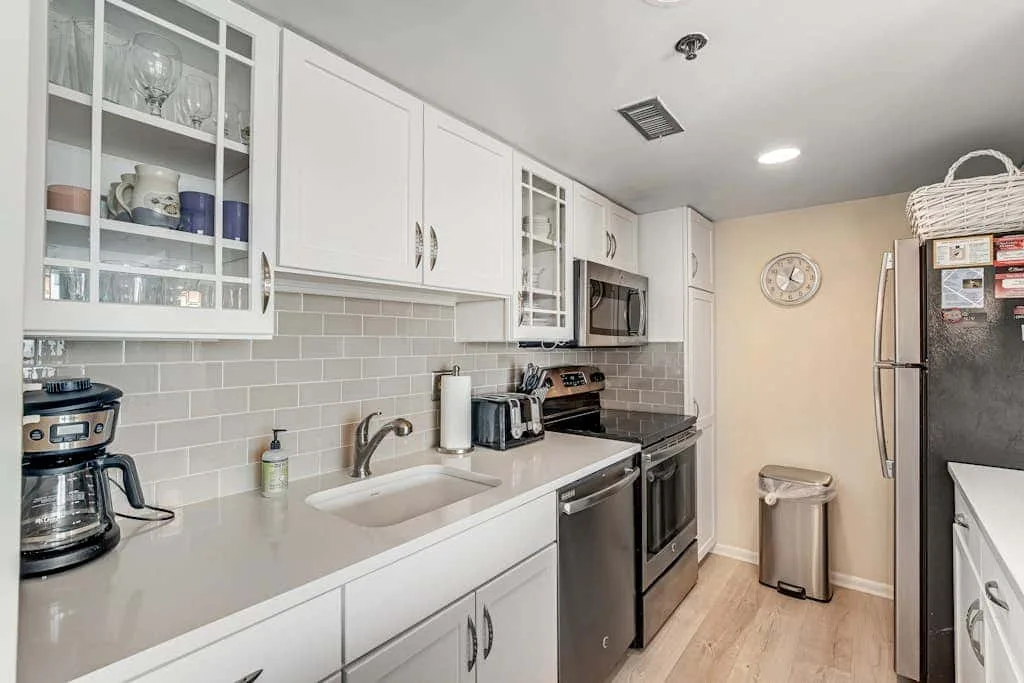 A bright kitchen with white cabinets, a long counter, and stainless steel appliances.