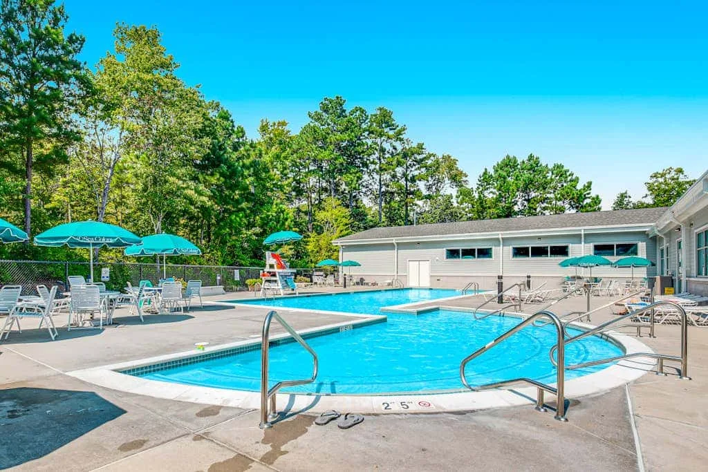 An outdoor swimming pool with metal handrails, patio seating, and trees.