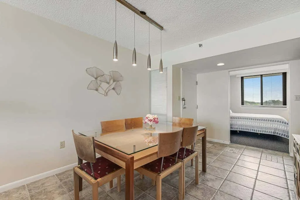 A dining area with a wooden table and pendant lights.