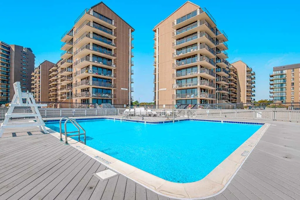 An outdoor swimming pool sits among several modern apartment buildings.