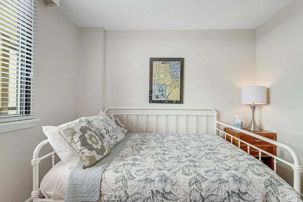 A bedroom with a metal bed, patterned bedding, and a lamp on a side table.