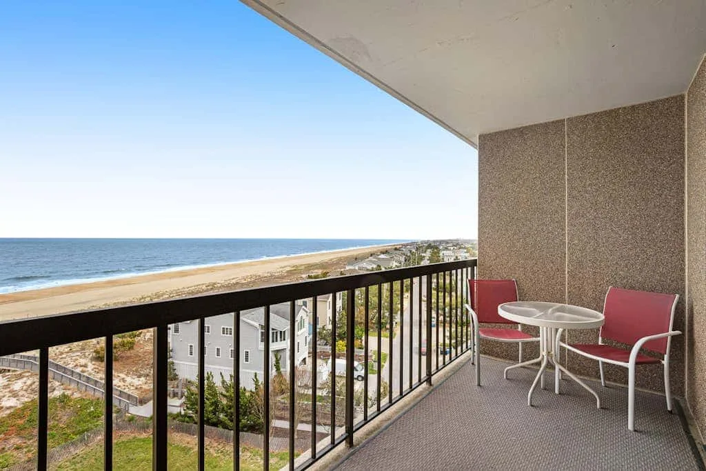 A balcony overlooks the ocean, with outdoor seating beside the railing.