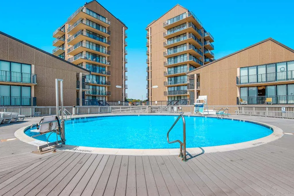 An outdoor swimming pool sits on a deck between several buildings.