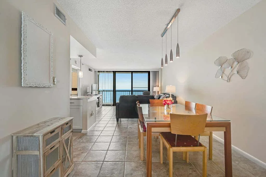 A bright open-plan living and dining area opens onto a balcony with an ocean view.