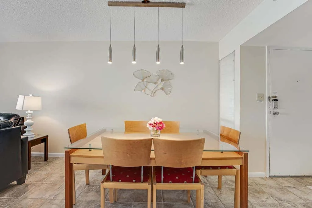 A dining area with a glass table, wooden chairs, and pendant lights.