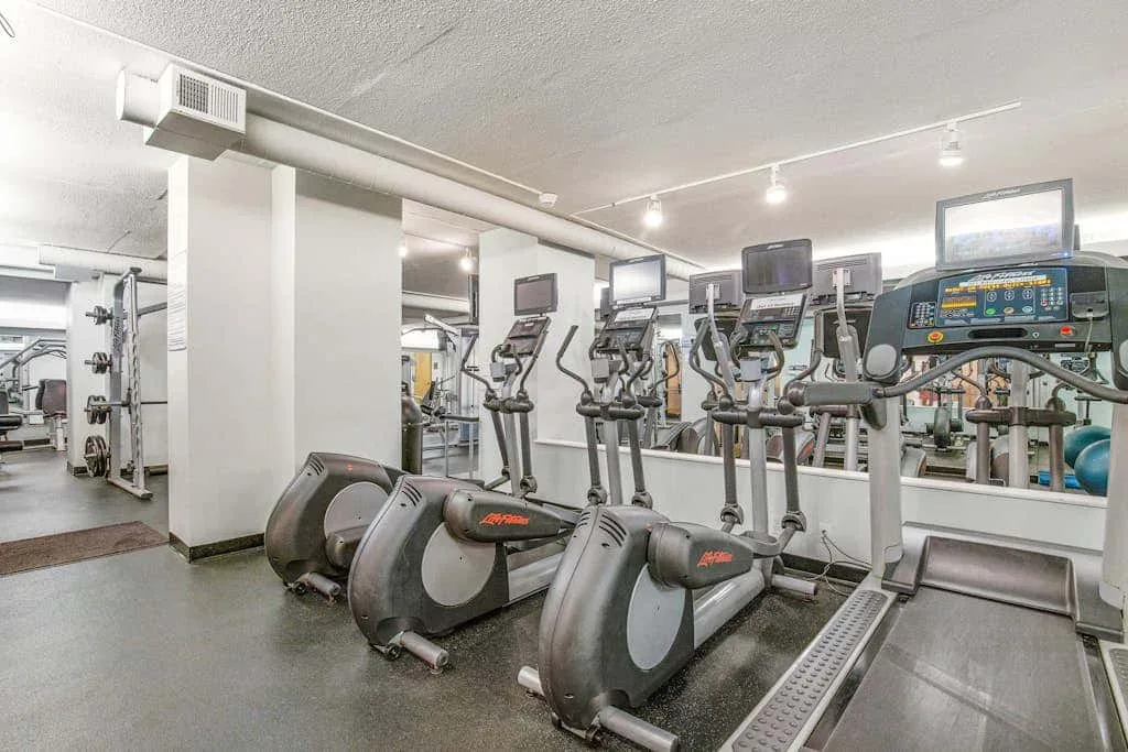 A fitness room with rows of cardio exercise machines and a mirrored wall.