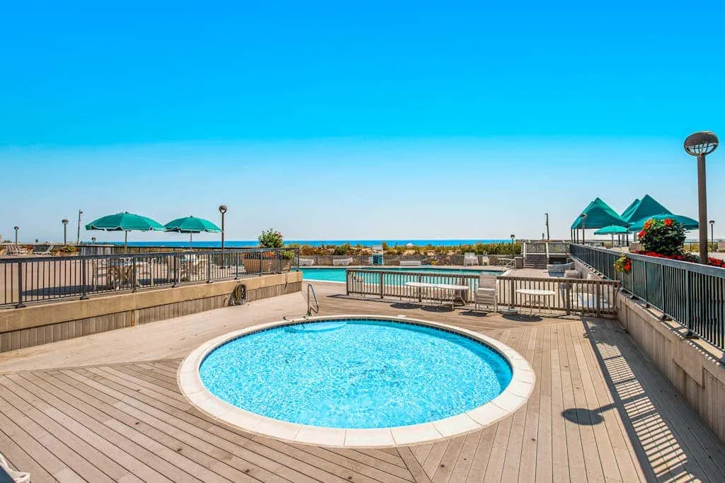 An outdoor pool sits on a wooden deck overlooking the sea.