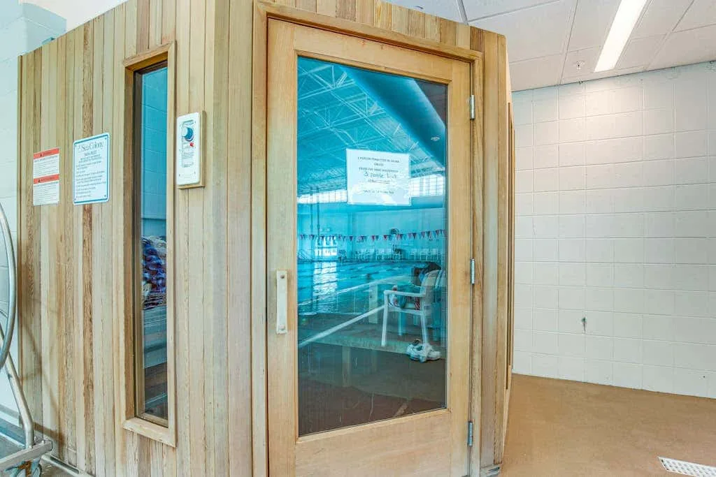A wooden sauna room with a glass door stands beside a tiled wall.