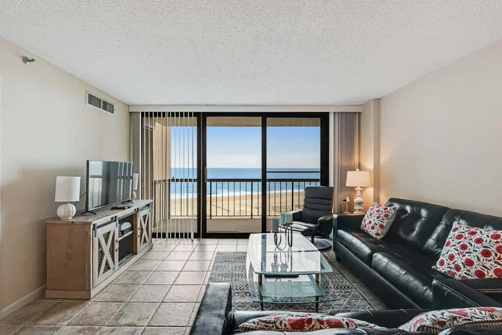 A living room with seating and a glass coffee table facing ocean views through sliding doors.