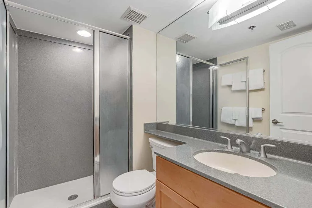 A bathroom vanity with a sink and mirror beside a shower.