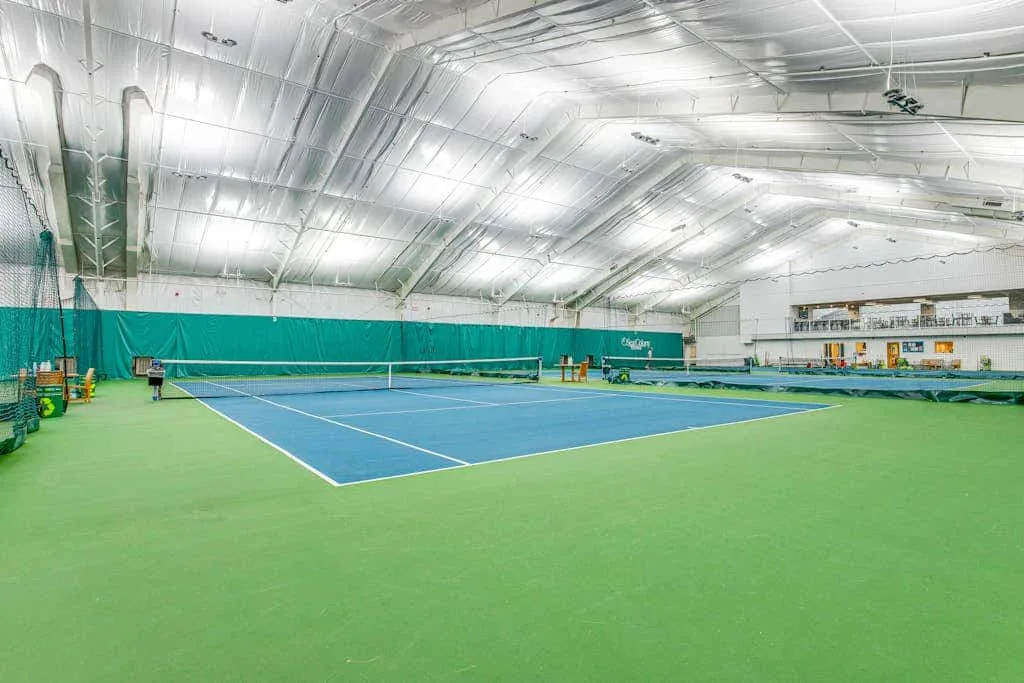 Indoor tennis court with blue playing surface and green surrounding area.