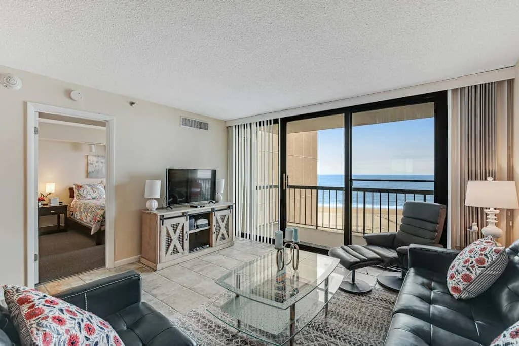 A living room with seating and a glass coffee table facing a balcony with an ocean view.