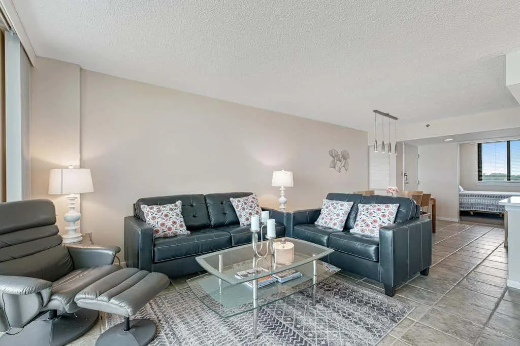 A living room with dark seating arranged around a glass coffee table.