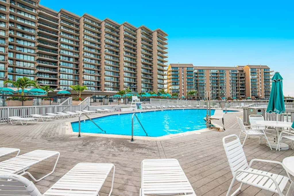 An outdoor swimming pool is surrounded by lounge chairs and tall residential buildings.