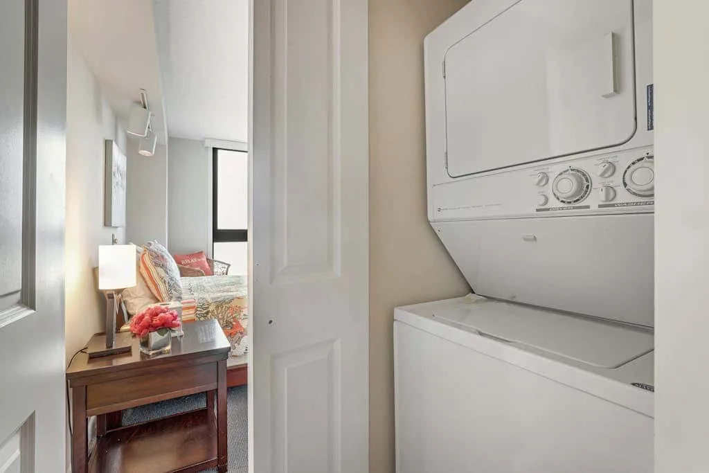 A bedroom is visible beside a stacked washer and dryer.