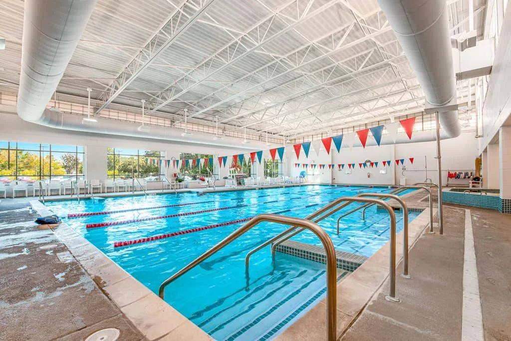 An indoor swimming pool with lane ropes and metal handrails.