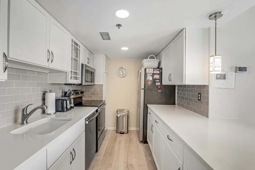 A bright kitchen with white cabinets, long counters, and a refrigerator.