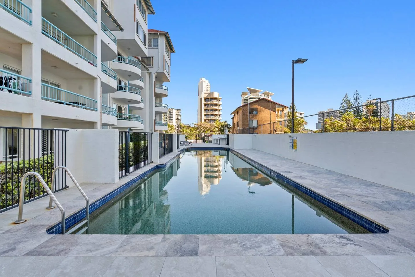 Una piscina exterior estrecha se extiende junto a un edificio de apartamentos moderno.