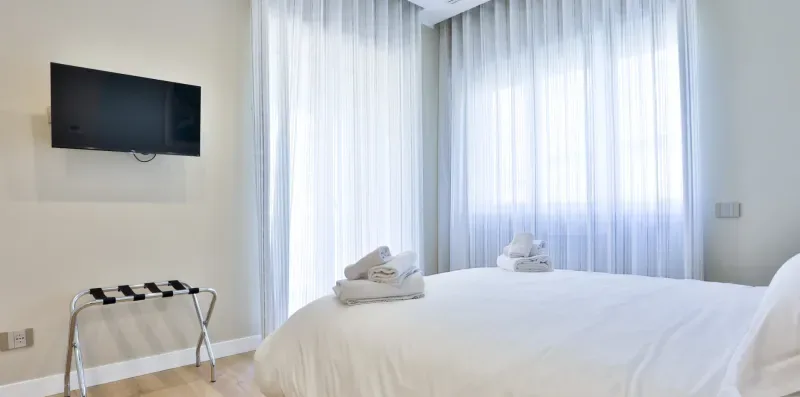 A bedroom with a neatly made bed and sheer curtains covering the windows.