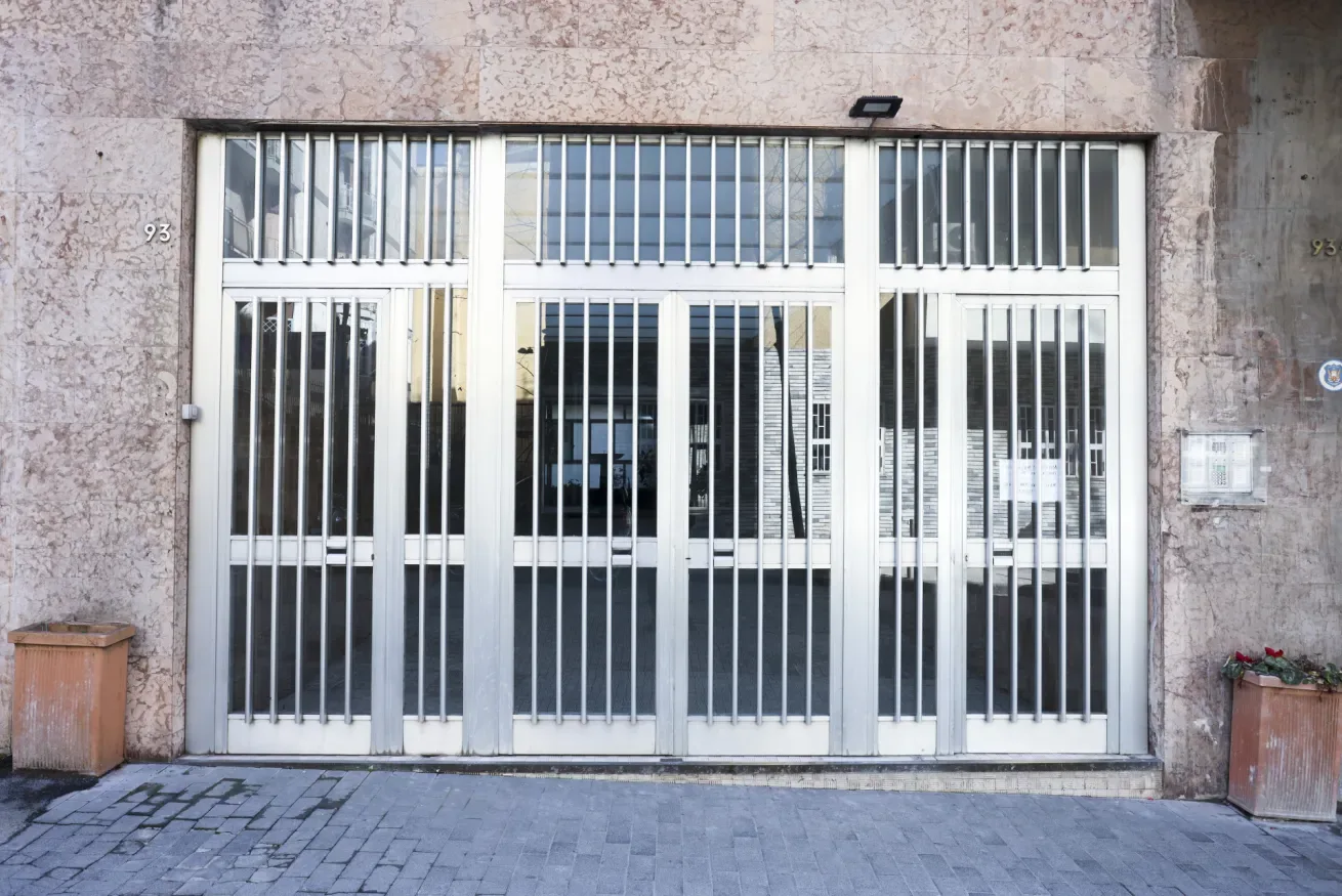 A barred glass entrance set into a stone facade above a paved sidewalk.