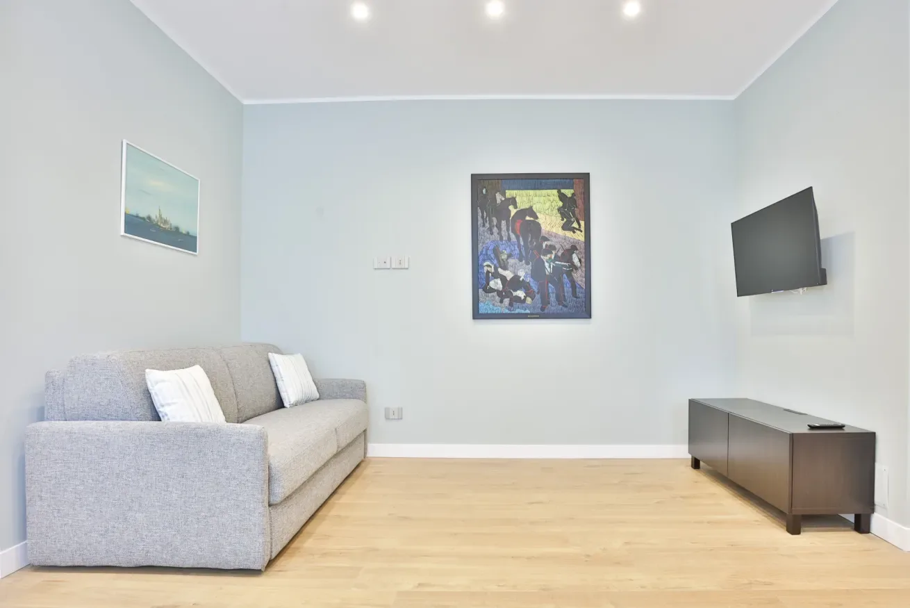 A living room with a gray sofa and a television mounted on the wall.