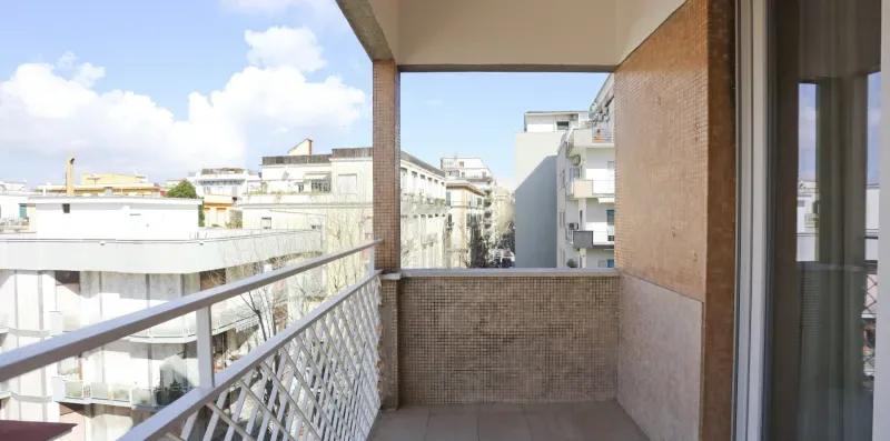 A covered balcony overlooks nearby buildings beneath a bright sky.