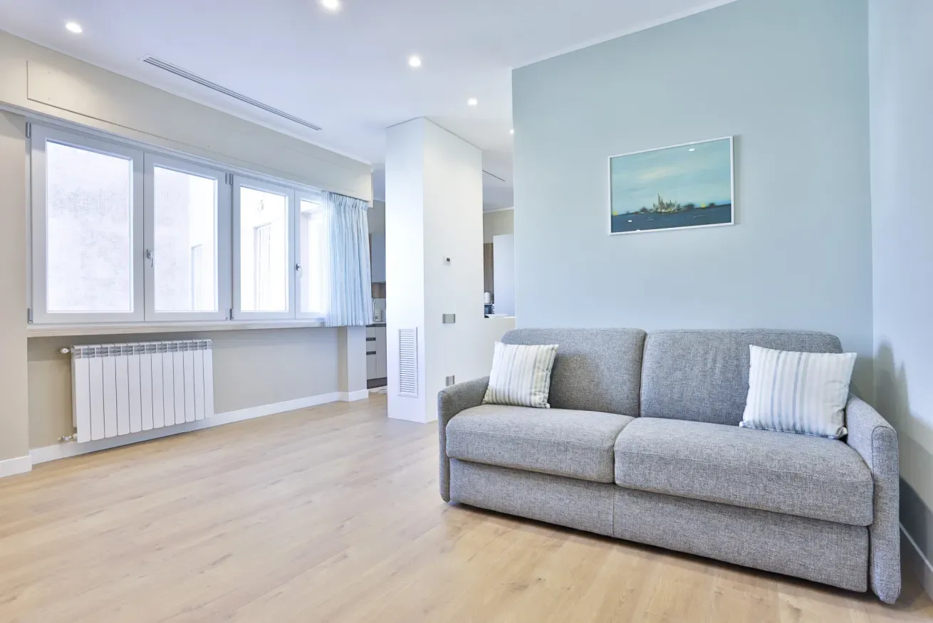 A bright living room with gray seating and a row of large windows.